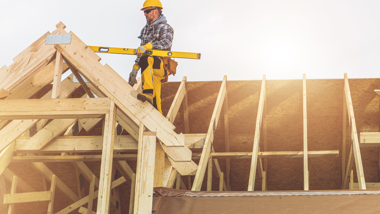 Construction worker leveling roof rafters with a yellow level. Bright sunlight.