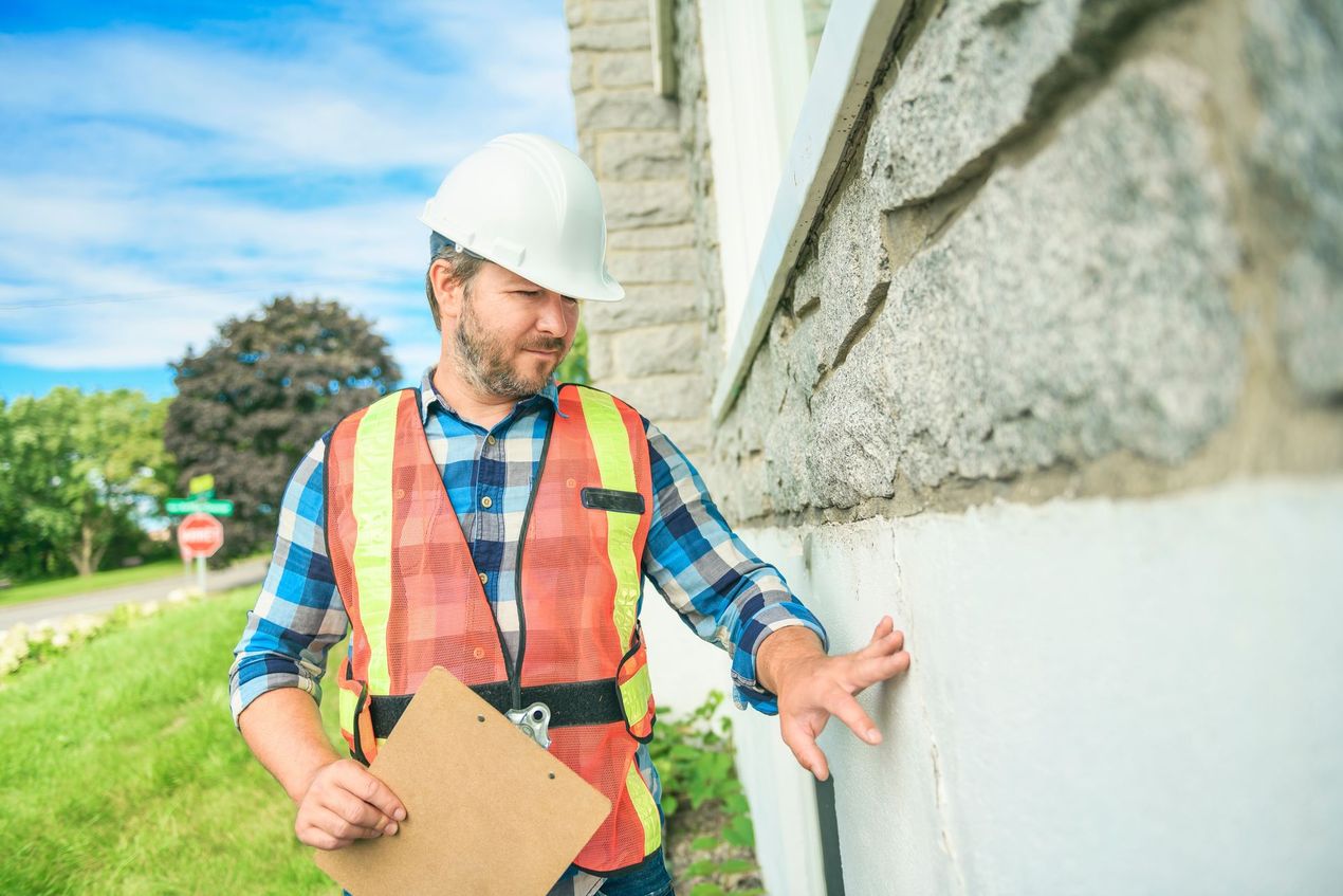 A man in a hard hat and vest is standing next to a building holding a clipboard.