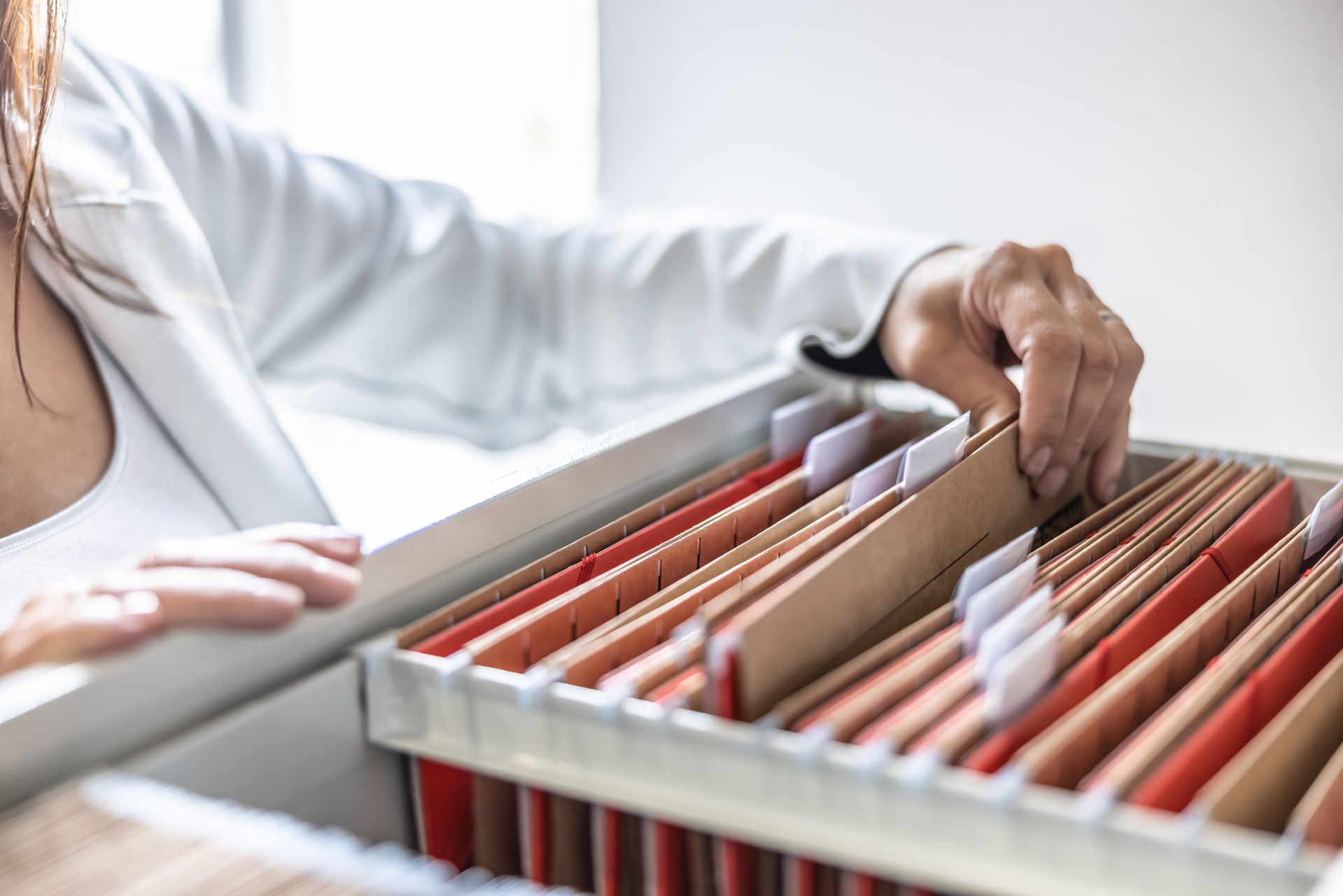 Person's hand reaching into a file cabinet, selecting a folder.  Many folders with tabs are visible.