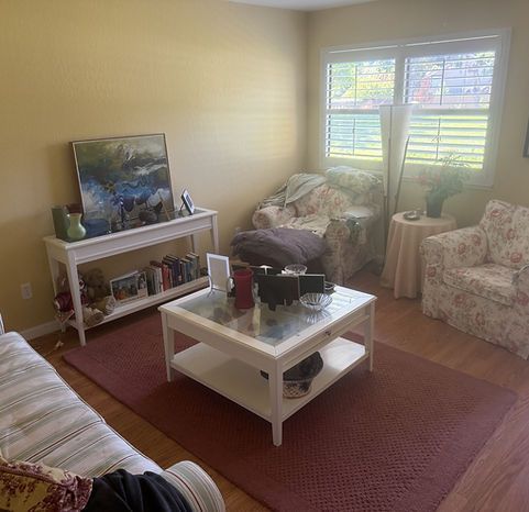Living room with white furniture, floral chairs, and a red rug.