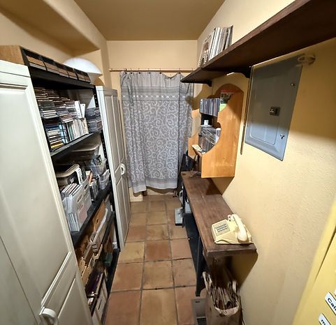 Narrow hallway with shelves, storage, and a telephone. Earth tones and a curtain at the end.