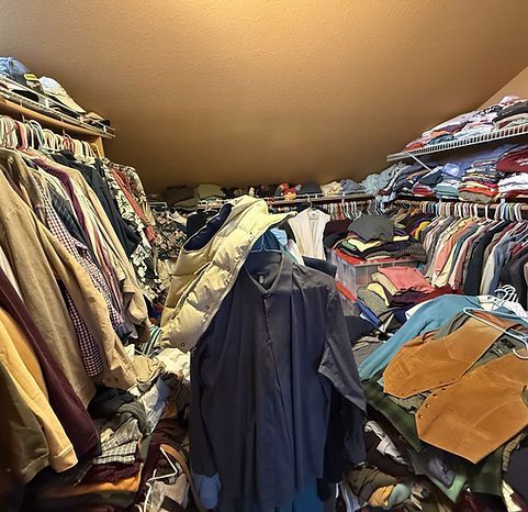A cluttered closet filled with clothes on hangers and shelves. Beige walls and ceiling.