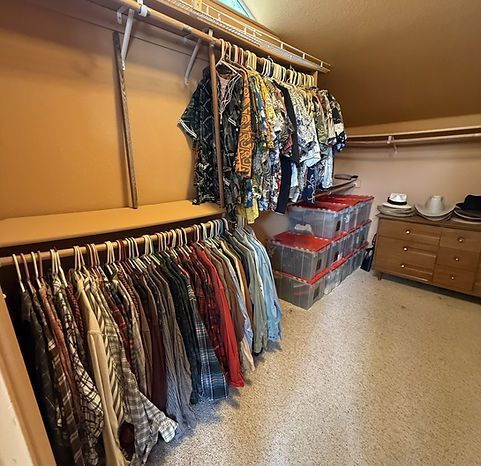 Walk-in closet with clothes hanging on rods, storage bins, and a wooden dresser.