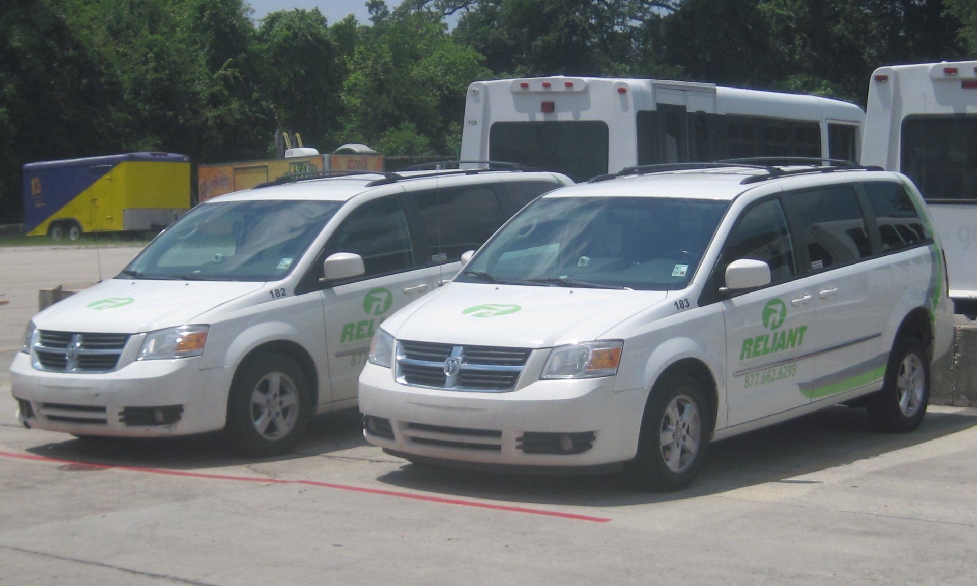 Two white Dodge Grand Caravan minivans parked outside, each with green logo and text on the side.