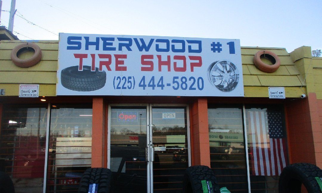 Sherwood #1 Tire Shop storefront with sign, phone number, and American flag. Exterior with orange accents and tires displayed.