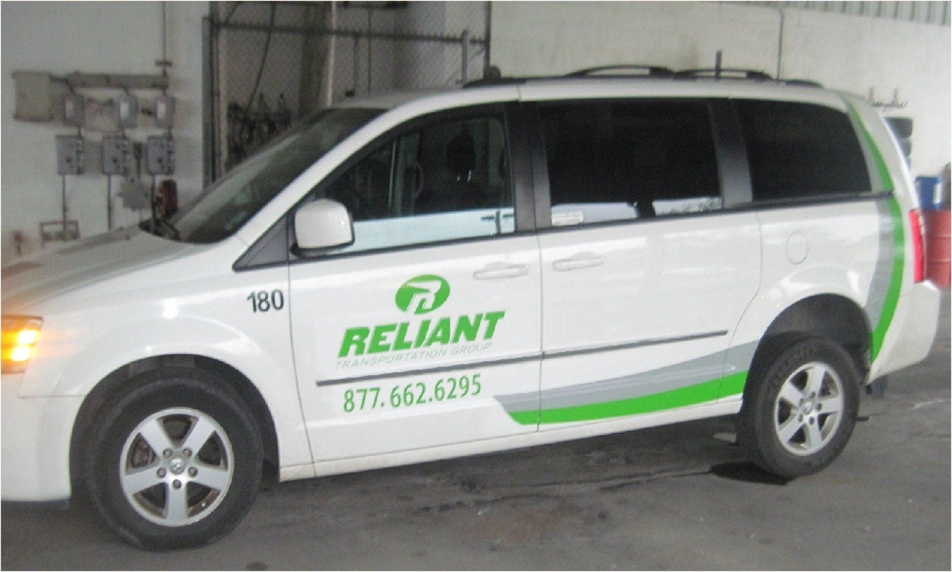 White Reliant minivan with green and gray accents parked in a garage. Phone number is visible on the side.