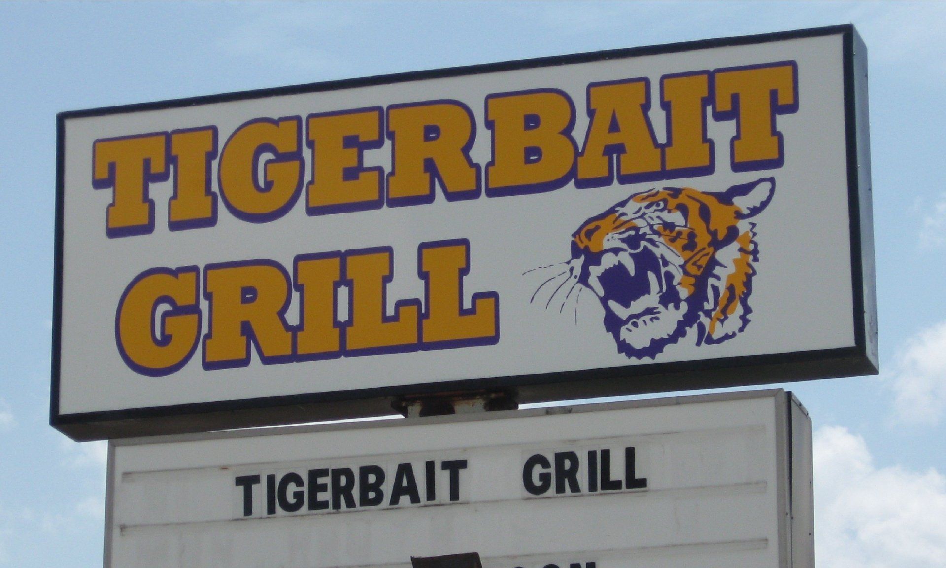 Sign for Tigerbait Grill; features orange text and tiger graphic on a white background. A second, smaller sign below has the same restaurant name.
