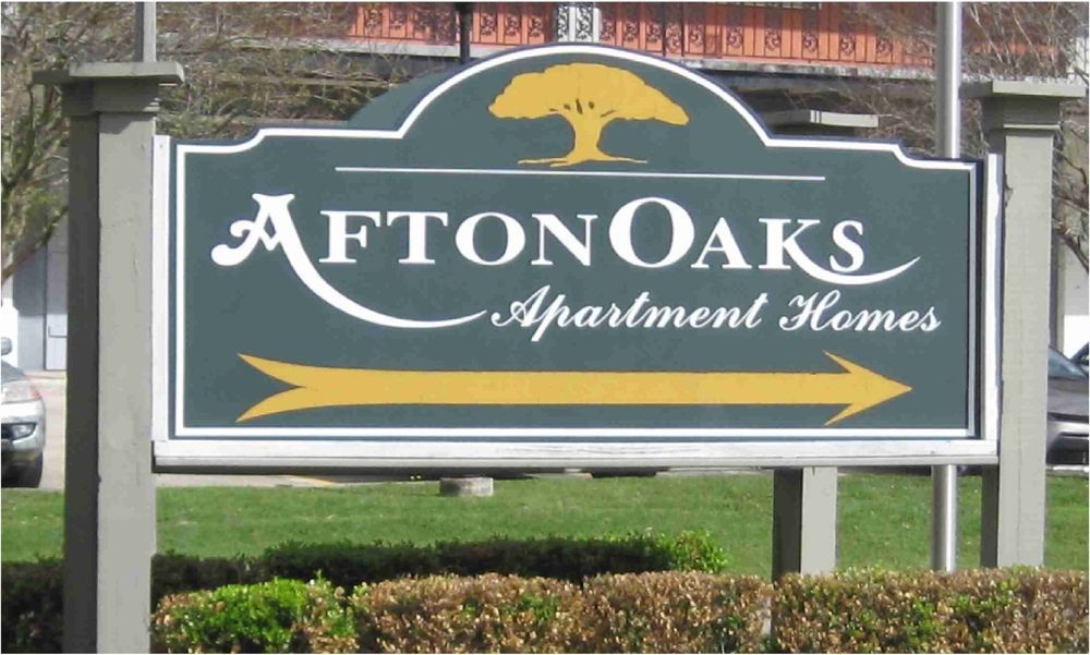 Sign for Afton Oaks Apartment Homes, green and white with a gold arrow. A tree graphic sits at the top.