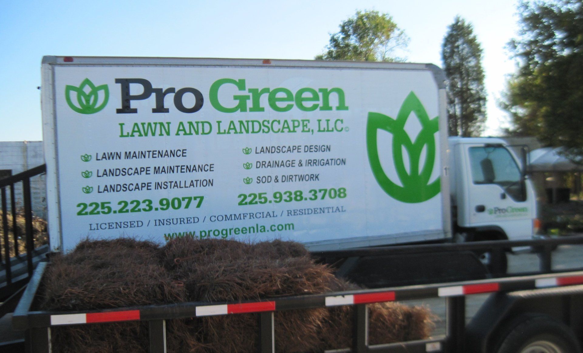 Pro Green Lawn and Landscape truck with logo and services listed, parked next to a trailer loaded with brown mulch.