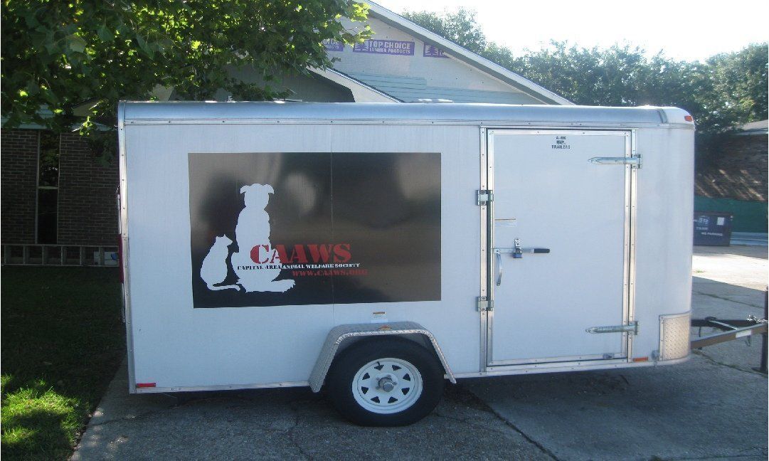 White trailer with a logo on the side featuring a dog and cat silhouette. It's parked outside, with a building visible in the background.