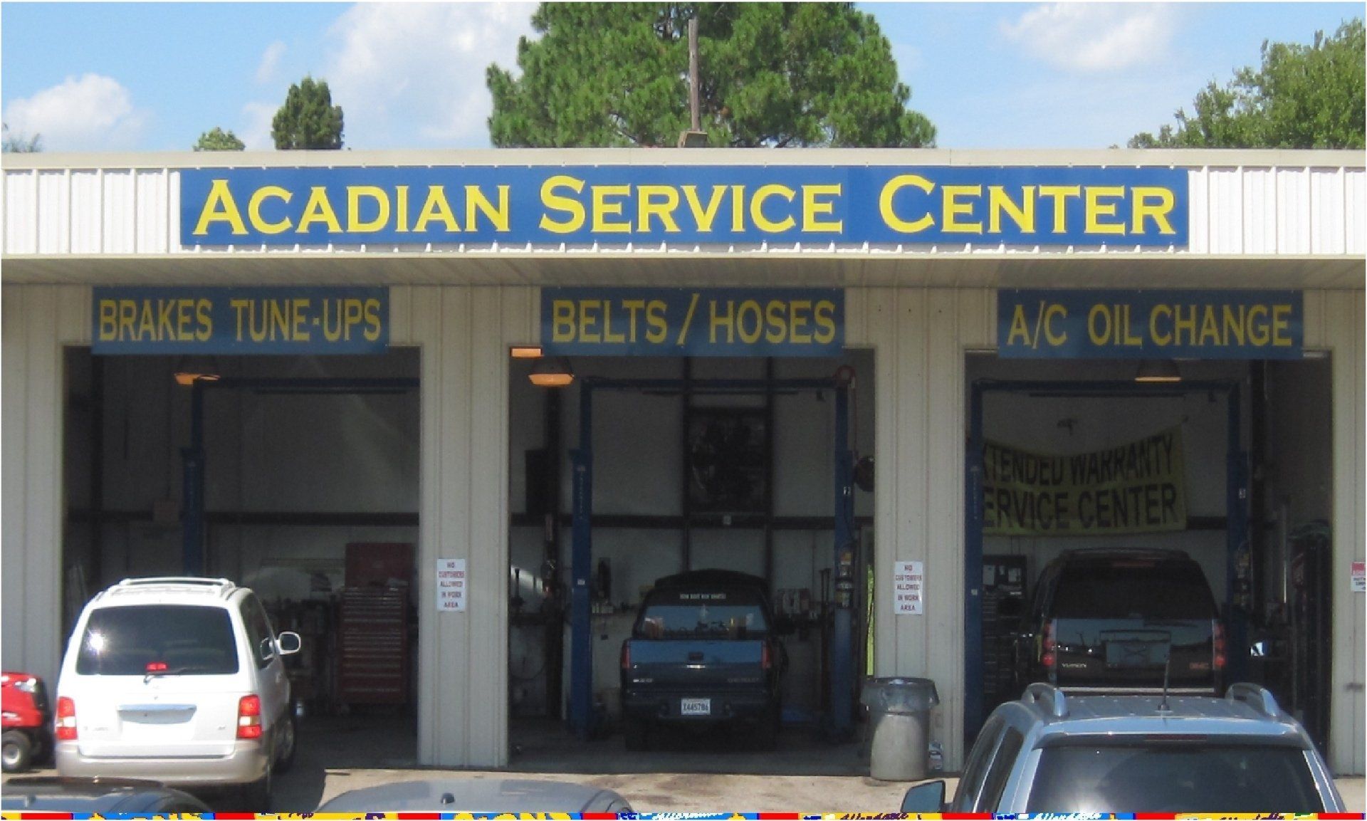 Acadian Service Center with bays for automotive work. Signage lists services: brakes, tune-ups, belts, hoses, A/C, and oil changes.