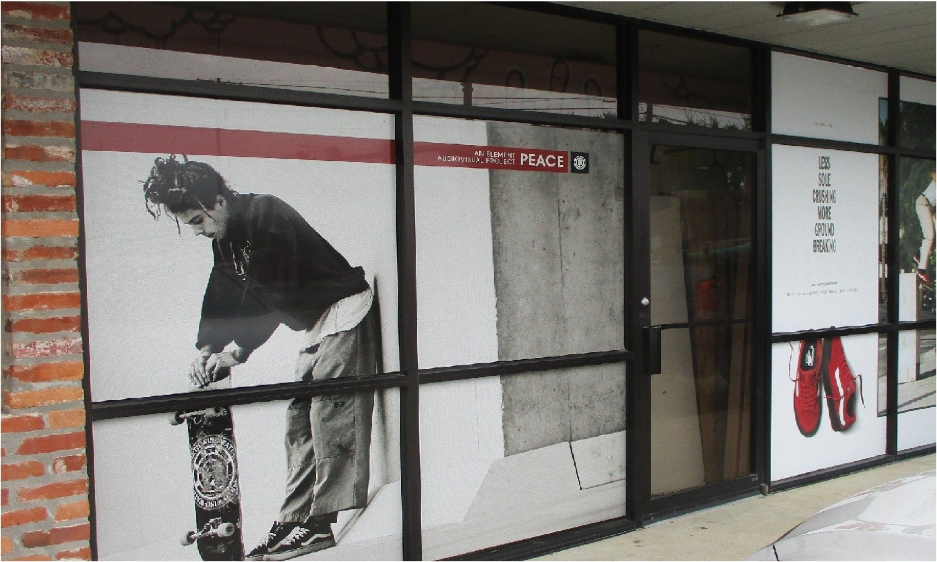 A storefront with large window decals. One shows a black and white image of a person with a skateboard. Red shoes are on another decal.