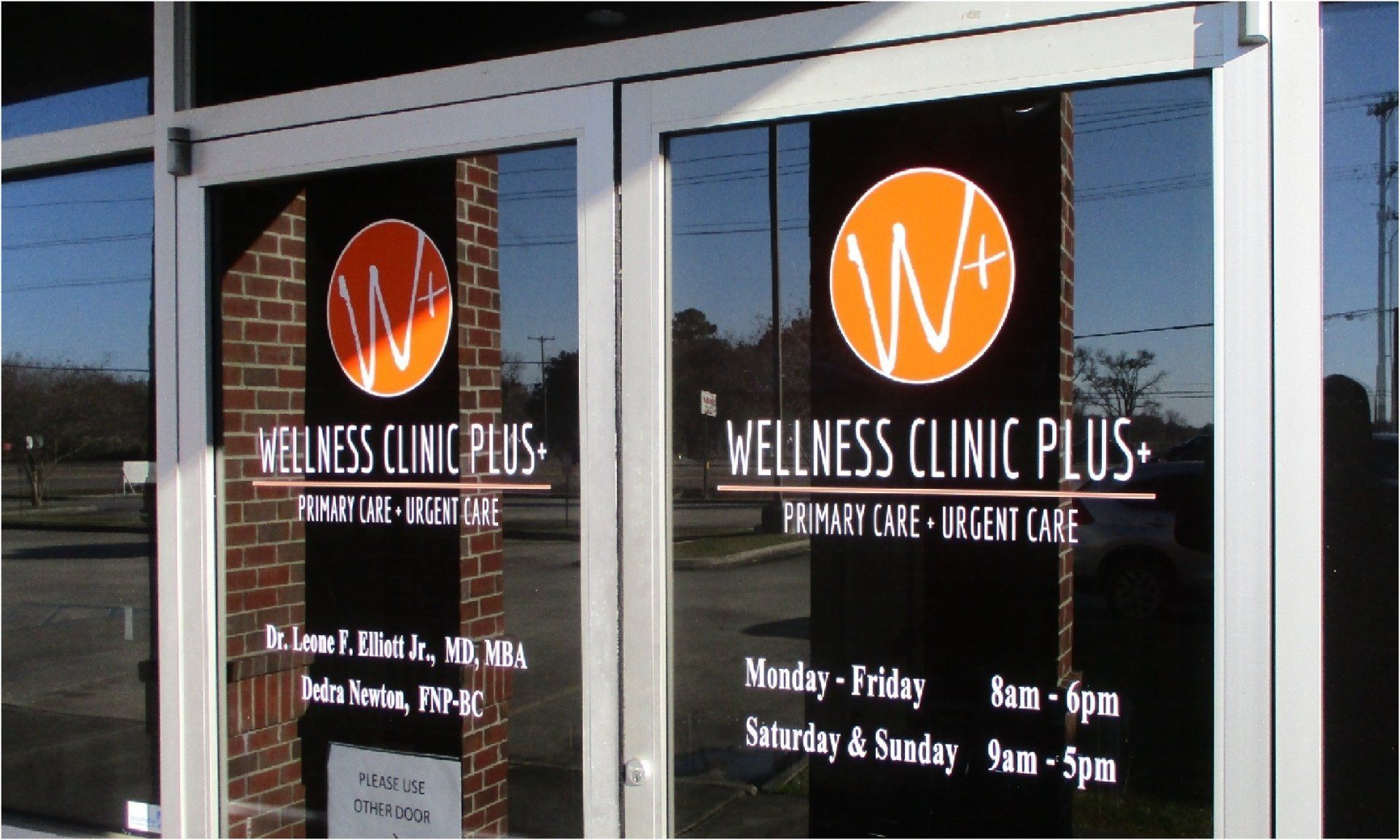 Glass doors of Wellness Clinic Plus with orange and white logo and text 
