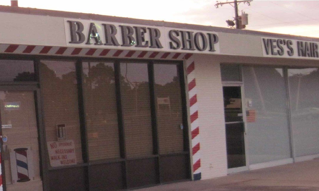 Barber shop storefront with a red and white striped barber pole. The sign reads 