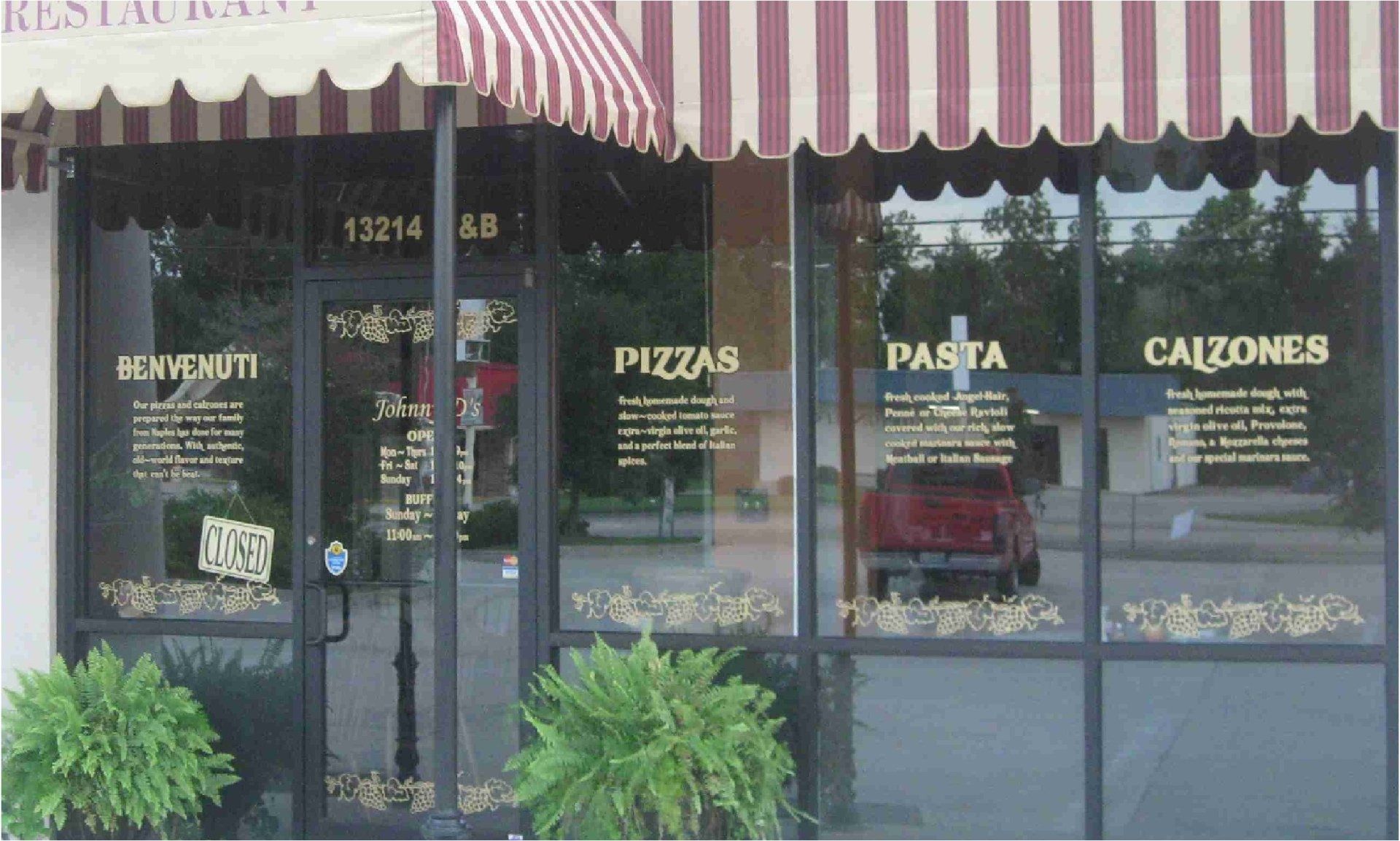 Exterior of an Italian restaurant with glass windows displaying menu items: pizzas, pasta, and calzones. A red pickup truck is visible through a window.