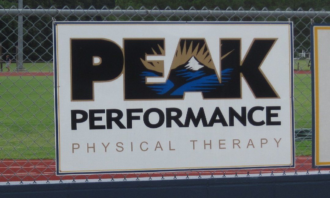 Sign for Peak Performance Physical Therapy, featuring the company name and logo with mountain imagery, outdoors.