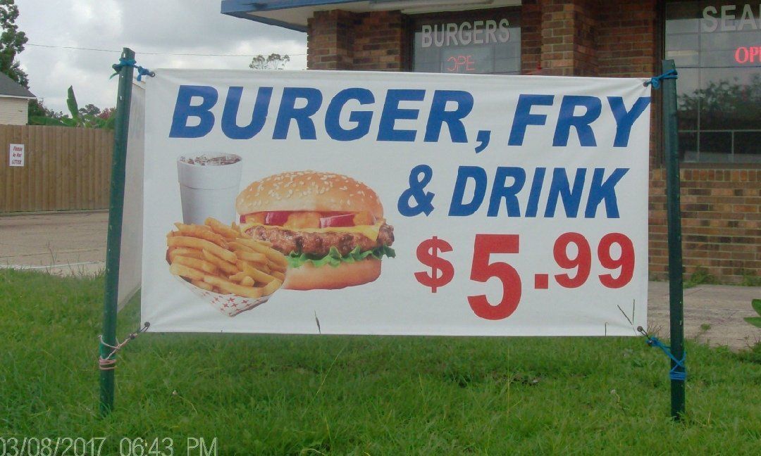 Sign for a burger, fry, and drink combo for $5.99, featuring a burger, fries, and a drink on a white banner in front of a brick building.