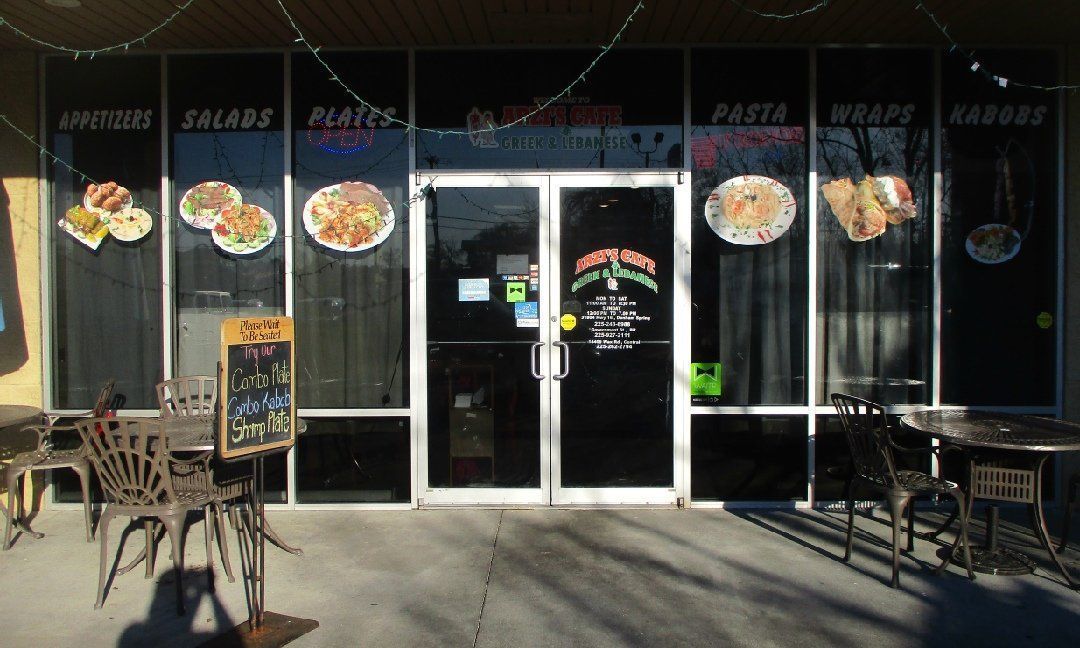 Exterior of a restaurant with glass doors and windows, featuring menu items like salads and wraps, plus outdoor seating.