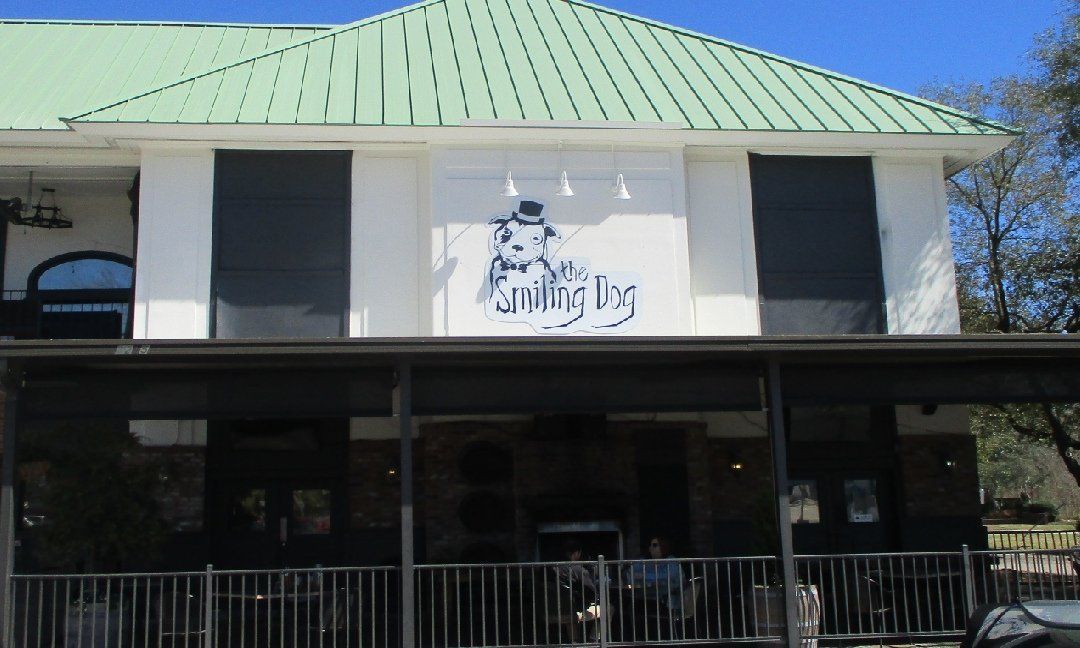 Smiling Dog restaurant exterior, two-story building with green roof and a sign featuring a cartoon dog. Black awnings and shutters on the building.