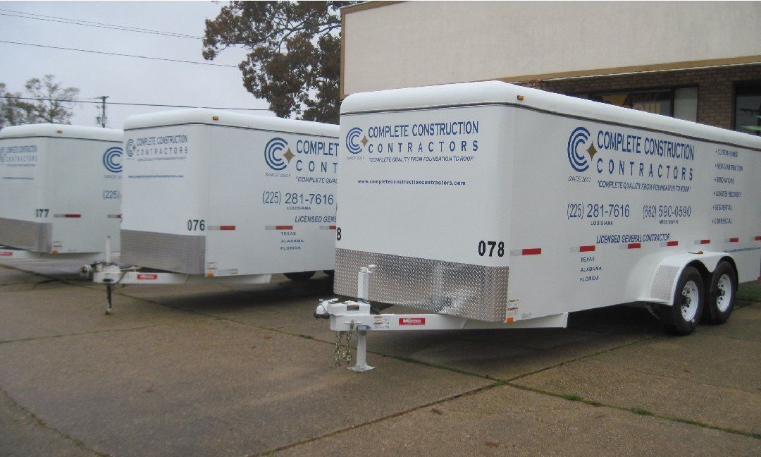 Three white trailers with blue logos are parked in front of a building. Each trailer has the same 