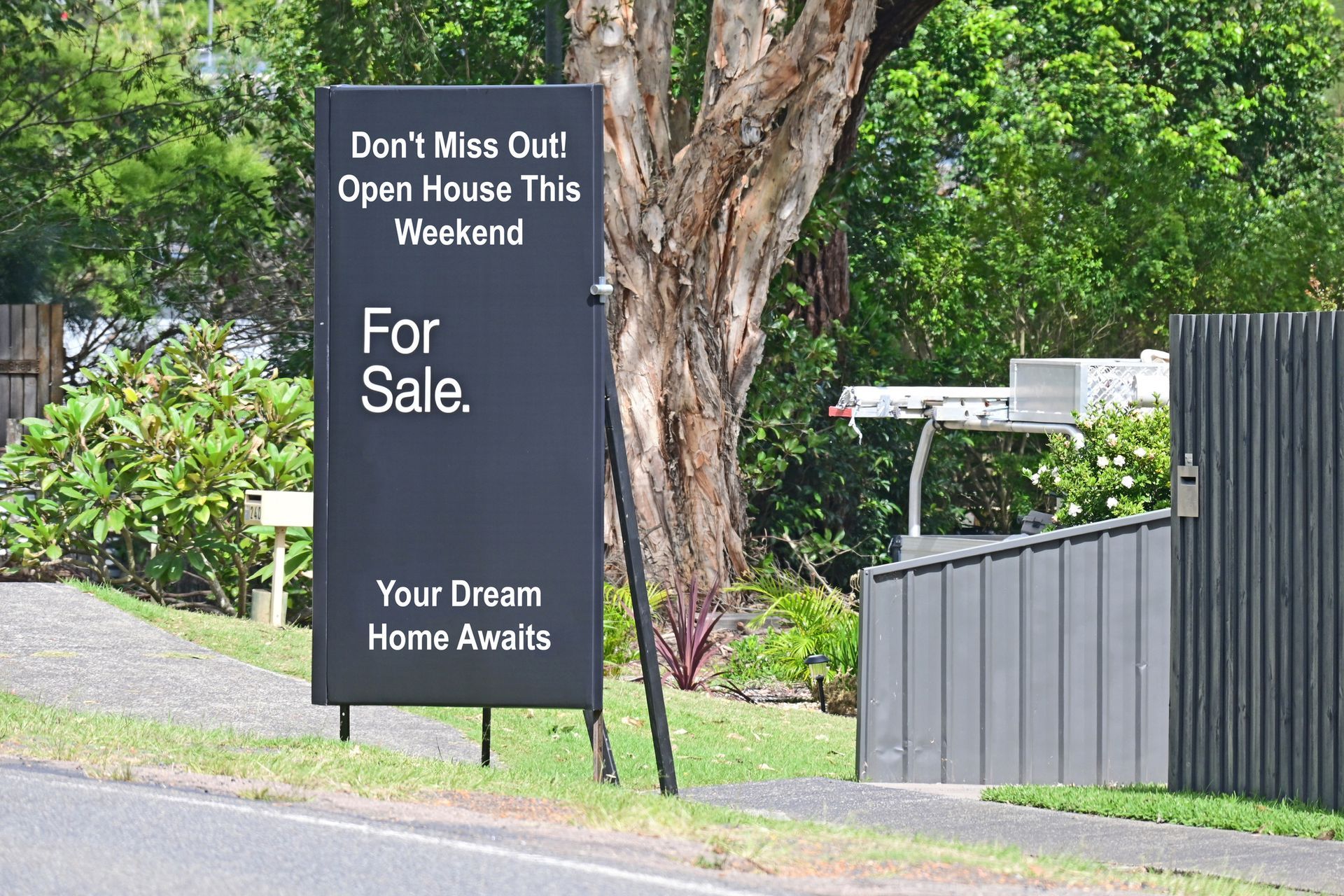 Black real estate sign on a street, advertising an open house. Text: 