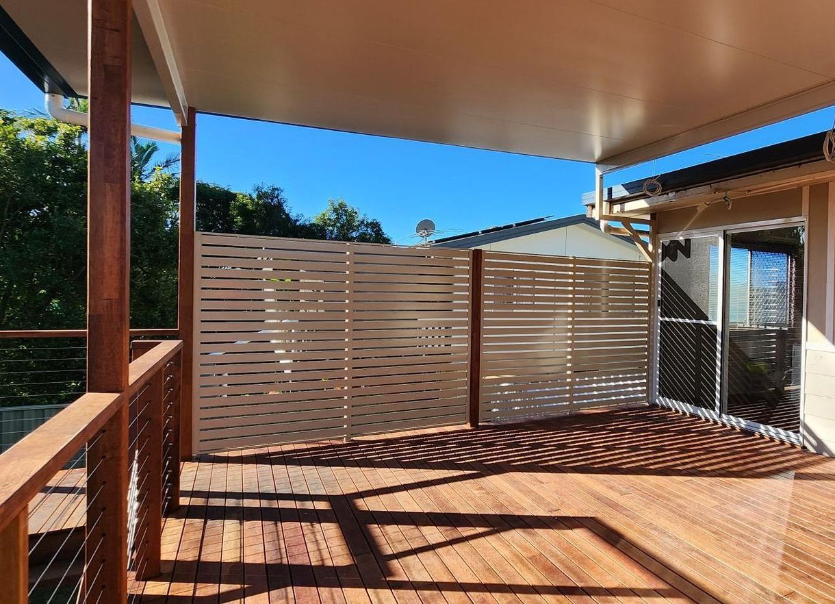 A privacy screen with red chair is sitting on a balcony overlooking a lush green field.