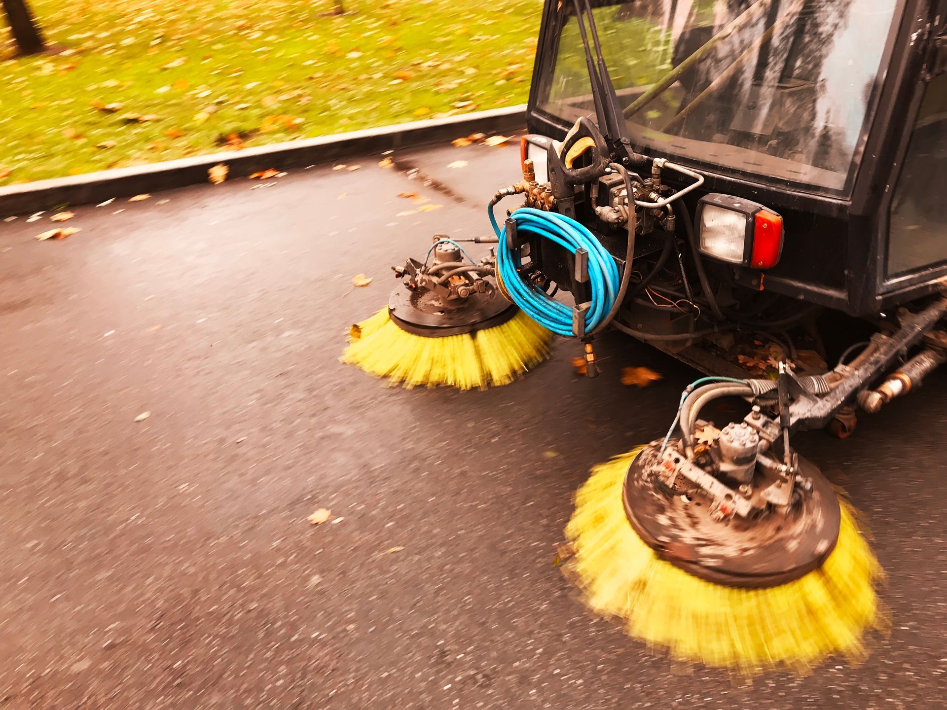 Eine Straßenkehrmaschine reinigt die Straße mit gelben Bürsten.