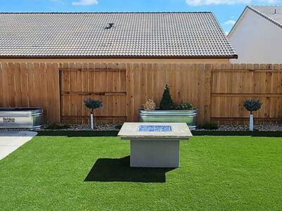 A fire pit is sitting on top of a lush green lawn in front of a wooden fence.