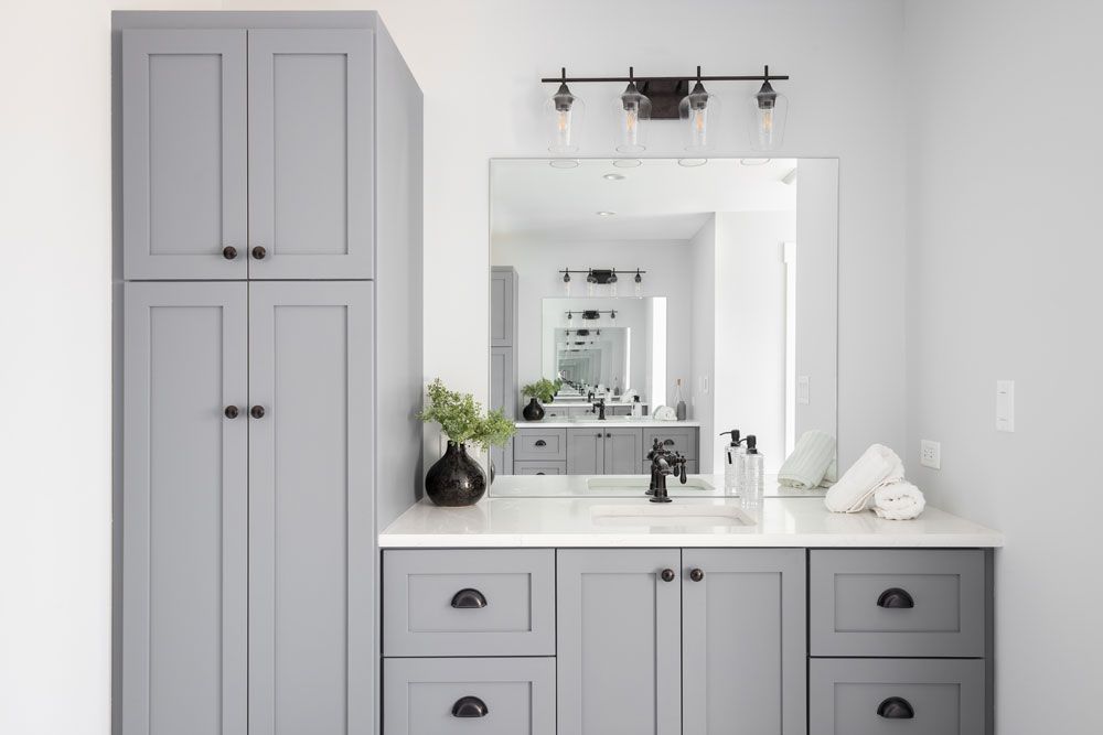 A bathroom with gray cabinets , a sink , and a mirror.