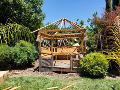 A wooden gazebo is being built in a backyard.