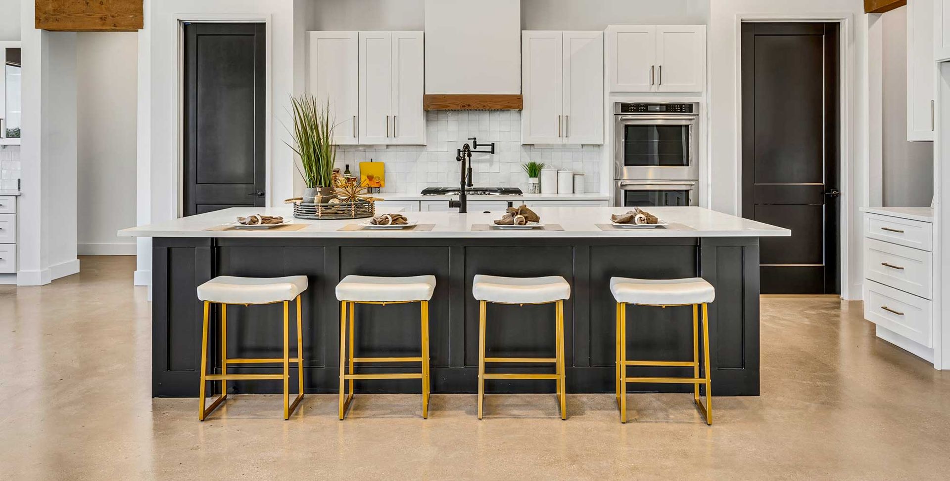 A kitchen with a large island , white cabinets , and gold stools.