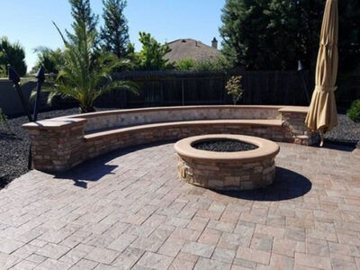 A brick patio with a fire pit and a bench