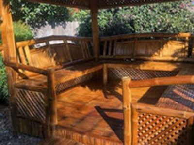 A wooden gazebo with a bench and a table in the middle of a garden.