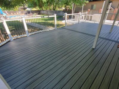 A gray deck with a white railing and a pool in the background.