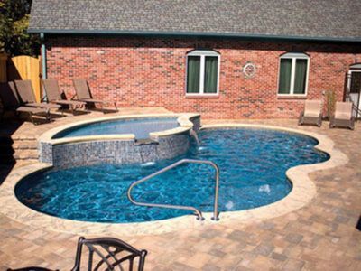 A large swimming pool with a hot tub in front of a brick house.