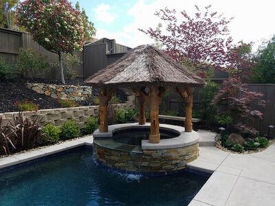 A gazebo with a thatched roof sits next to a swimming pool.