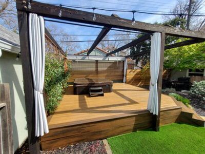 A wooden deck with a hot tub under a pergola in a backyard.