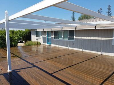 A wooden deck with a white canopy over it in front of a house.