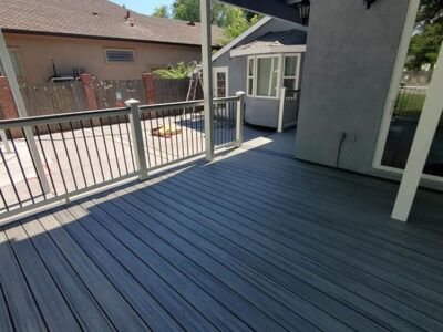 A gray deck with a white railing and a house in the background