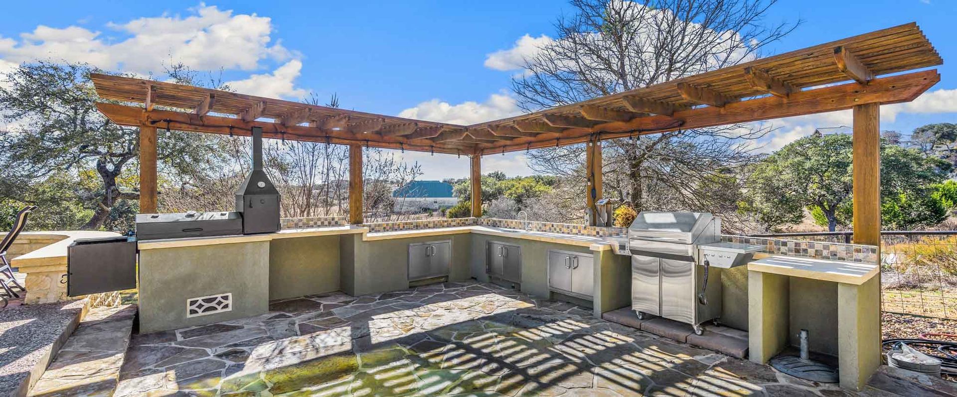 A large outdoor kitchen with a pergola and a grill.