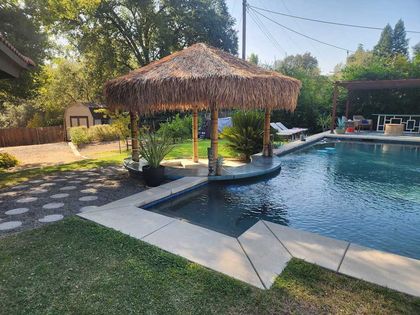 A swimming pool with a thatched umbrella in the middle of it.