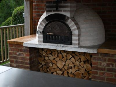 A brick oven is sitting next to a pile of wood.