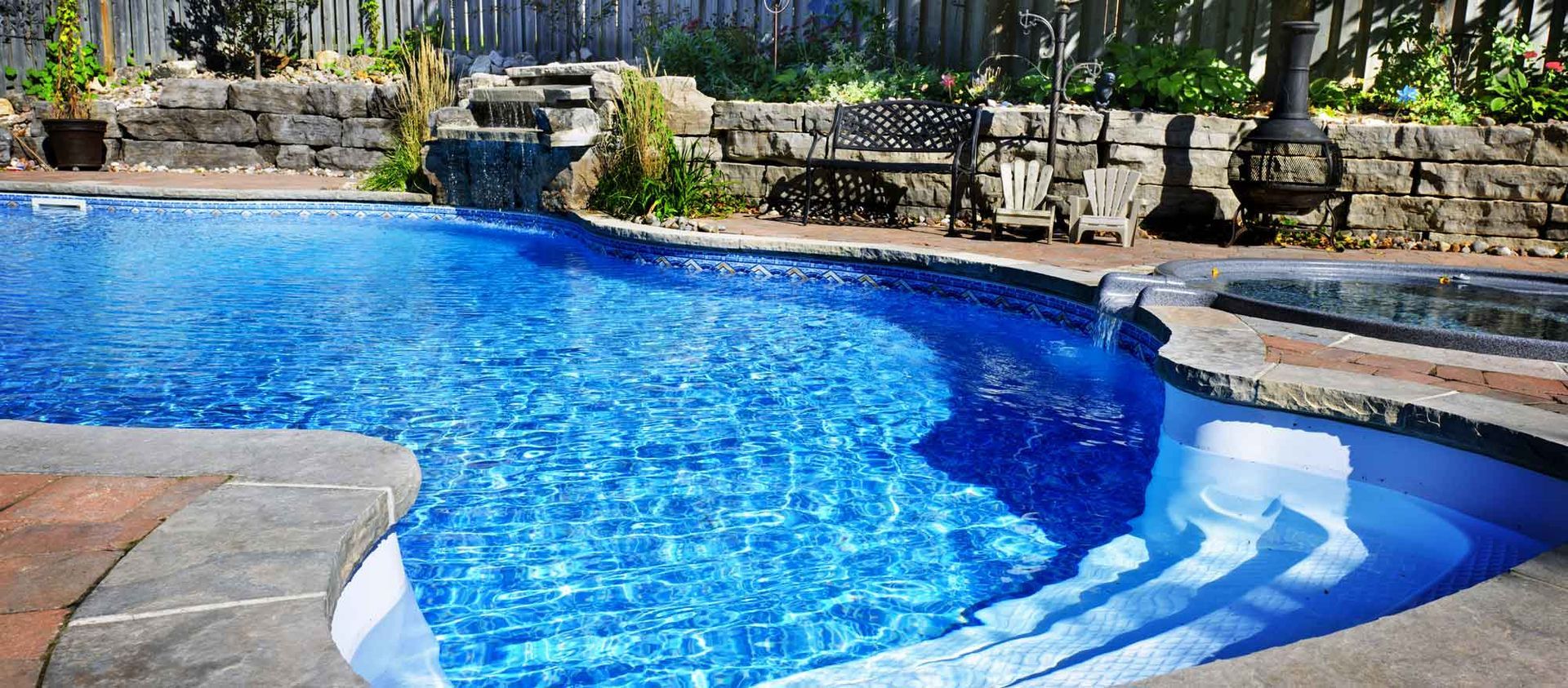 A large swimming pool with a waterfall in the backyard.