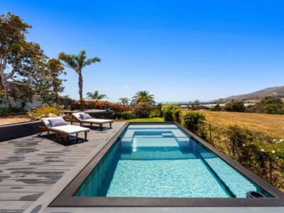 A large swimming pool is surrounded by chairs on a deck.