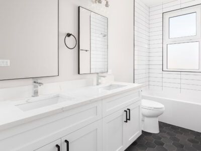 A bathroom with white cabinets , a toilet , a sink and a mirror.
