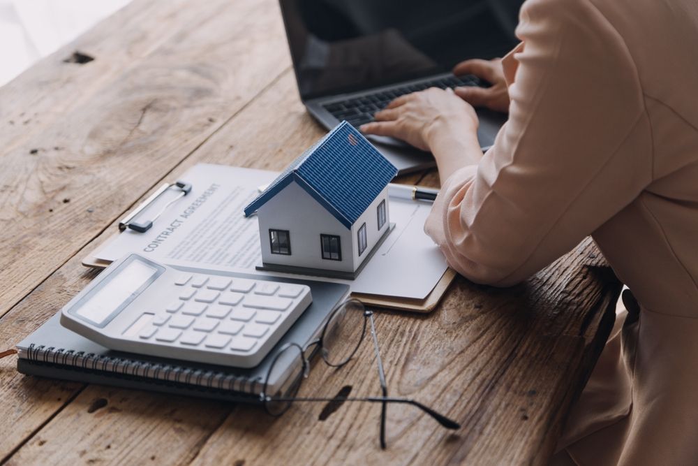 Woman focused on her laptop with a small house model displayed on the table beside her.