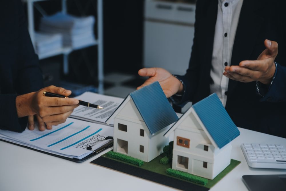 Real estate agent and client reviewing a house model during a discussion in a bright, modern office setting.