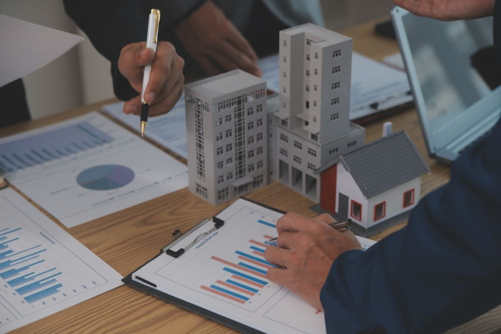Business professionals collaborating on a project, examining a house model on a table.