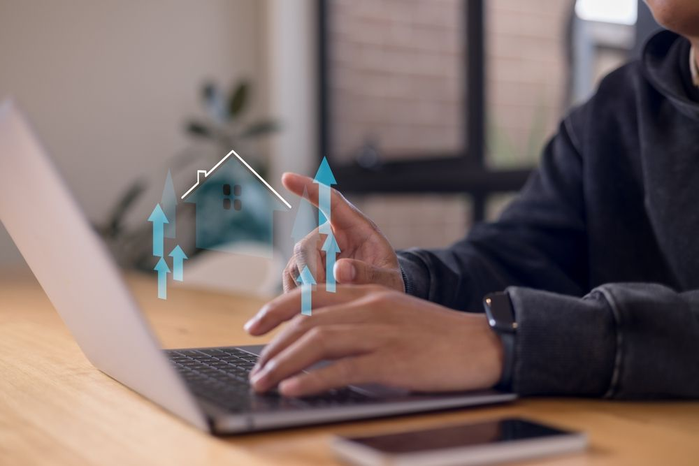 Man using a laptop displaying a house icon on the screen, focused on his work in a home office setting.