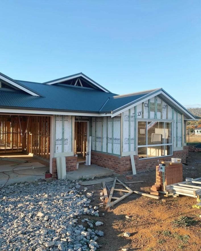 A House is Being Built With a Blue Roof and a Lot of Rocks in Front of It — Trussted Frames & Trusses In Taminda, NSW